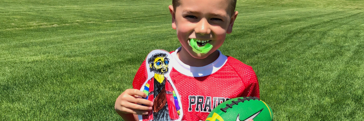 A boy smiles with his Flat Jesus on a football field | Sparkhouse Blog