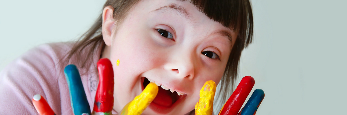 Girl with Down syndrome smiles while finger painting | Sparkhouse Blog