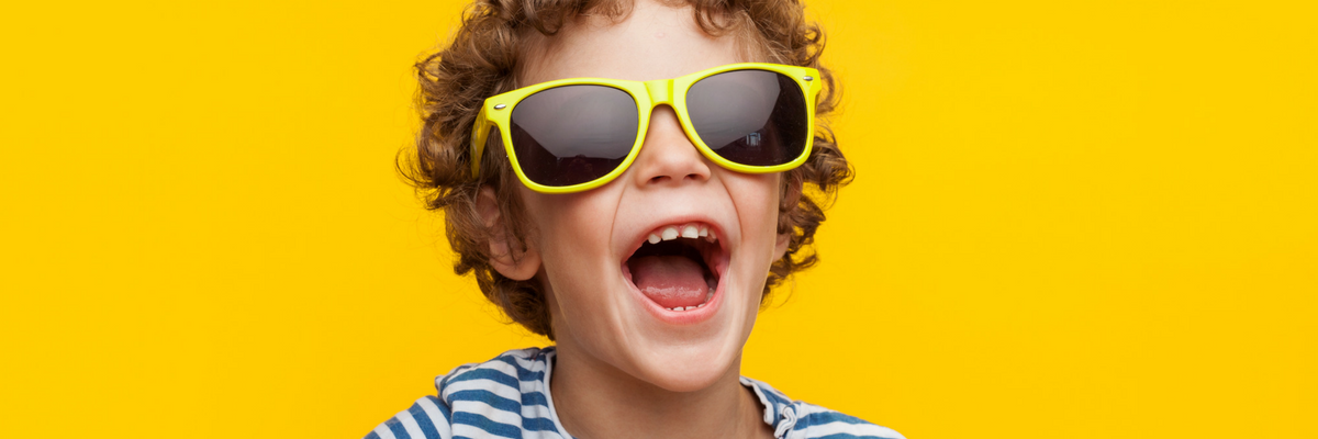 Kid wearing sunglasses laughs in front of summery yellow background | Sparkhouse Blog