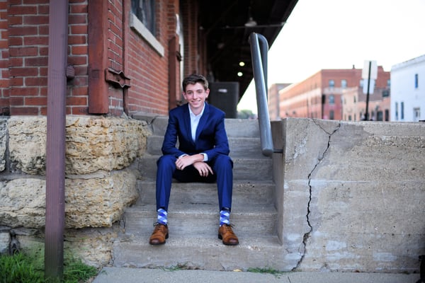 A boy in his late teens wearing a suit sitting on some stairs